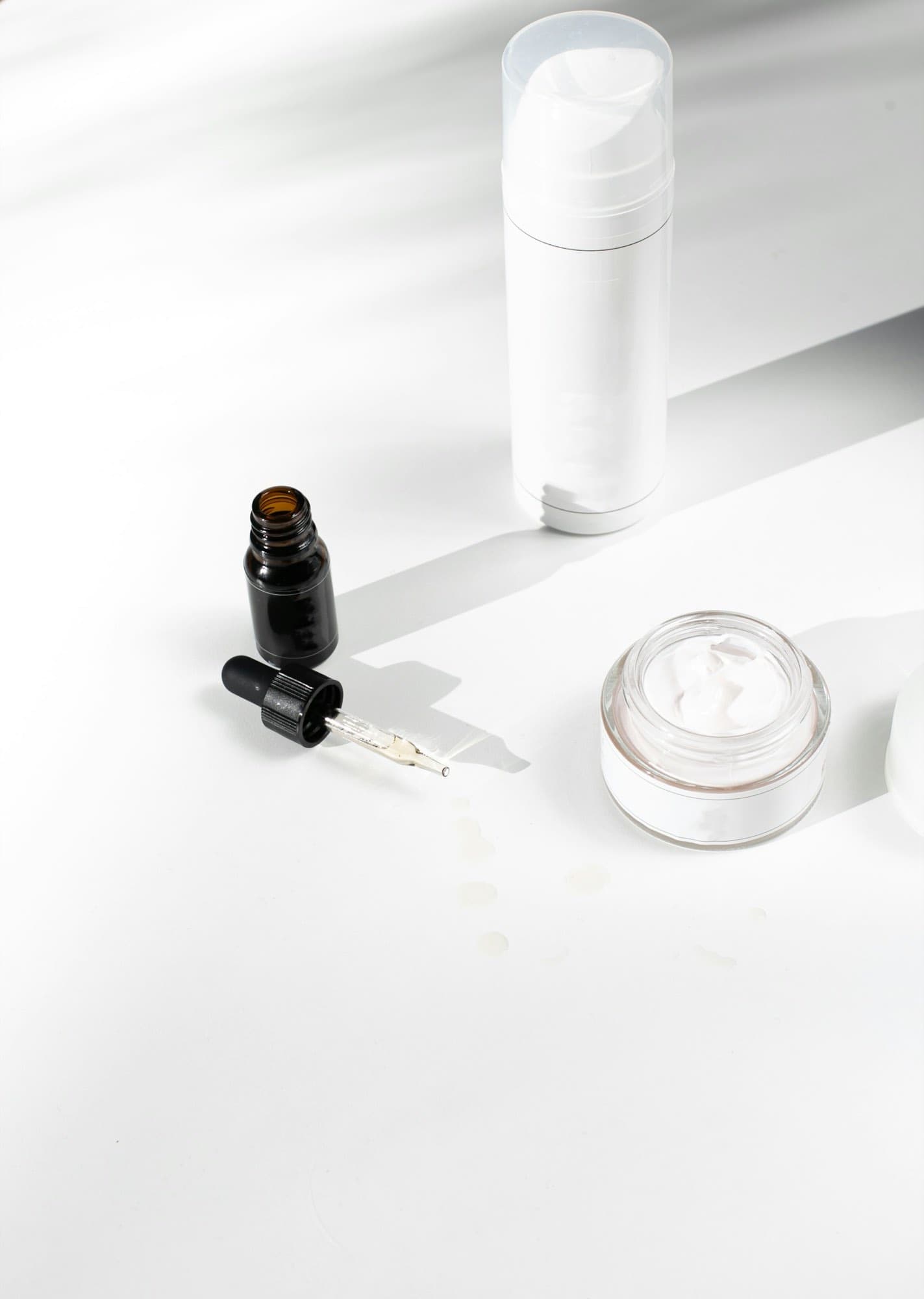 A serum bottle and an open jar of cream in hard daylight