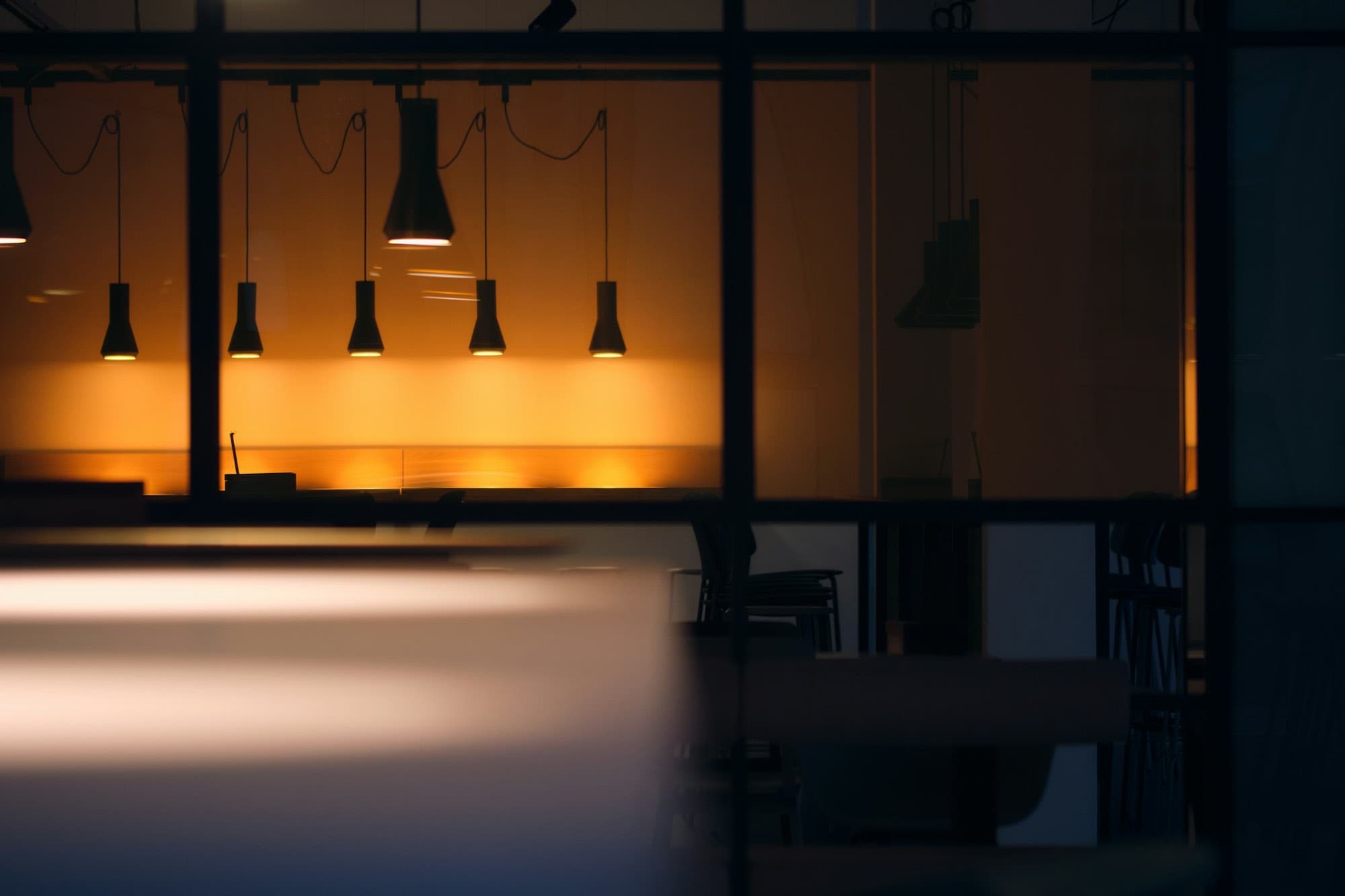 A dark bar interior lit by a row of warm pendant lamps