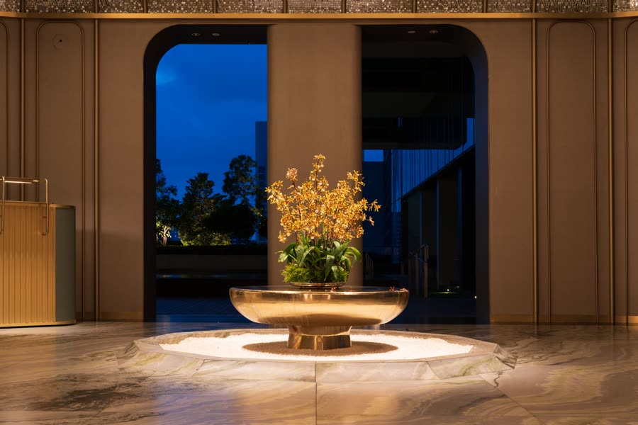 Eine Hotellobby bei Nacht: eine Bronzeschale mit Blumen in warmem Licht